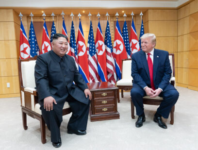 Kim Jong un and Donald Trump sit posing for photographs with US and North Korean flags in the background